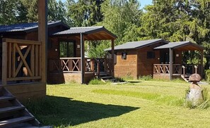 A wooden cabin with a porch, a fenced area, and a grassy yard.