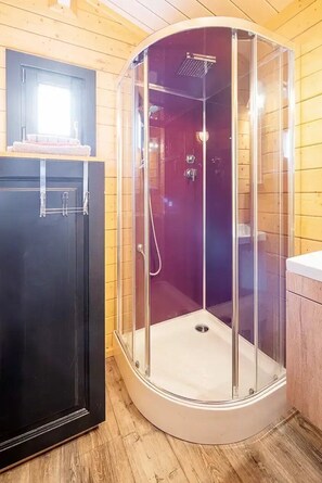 Une douche d’angle avec des parois en verre, un plancher en bois et un meuble noir.