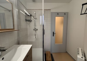 Moderni kylpyhuone, jossa on lasinen suihkuseinä, valkoinen pesuallas ja himmeäksi käsitelty lasipaneeli ovessa.