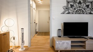A modern living room with a flat-screen TV, a standing heater, and a decorative wall piece. - Le Nid d'Alspach: Romantic Retreat in Colmar (Colmar)