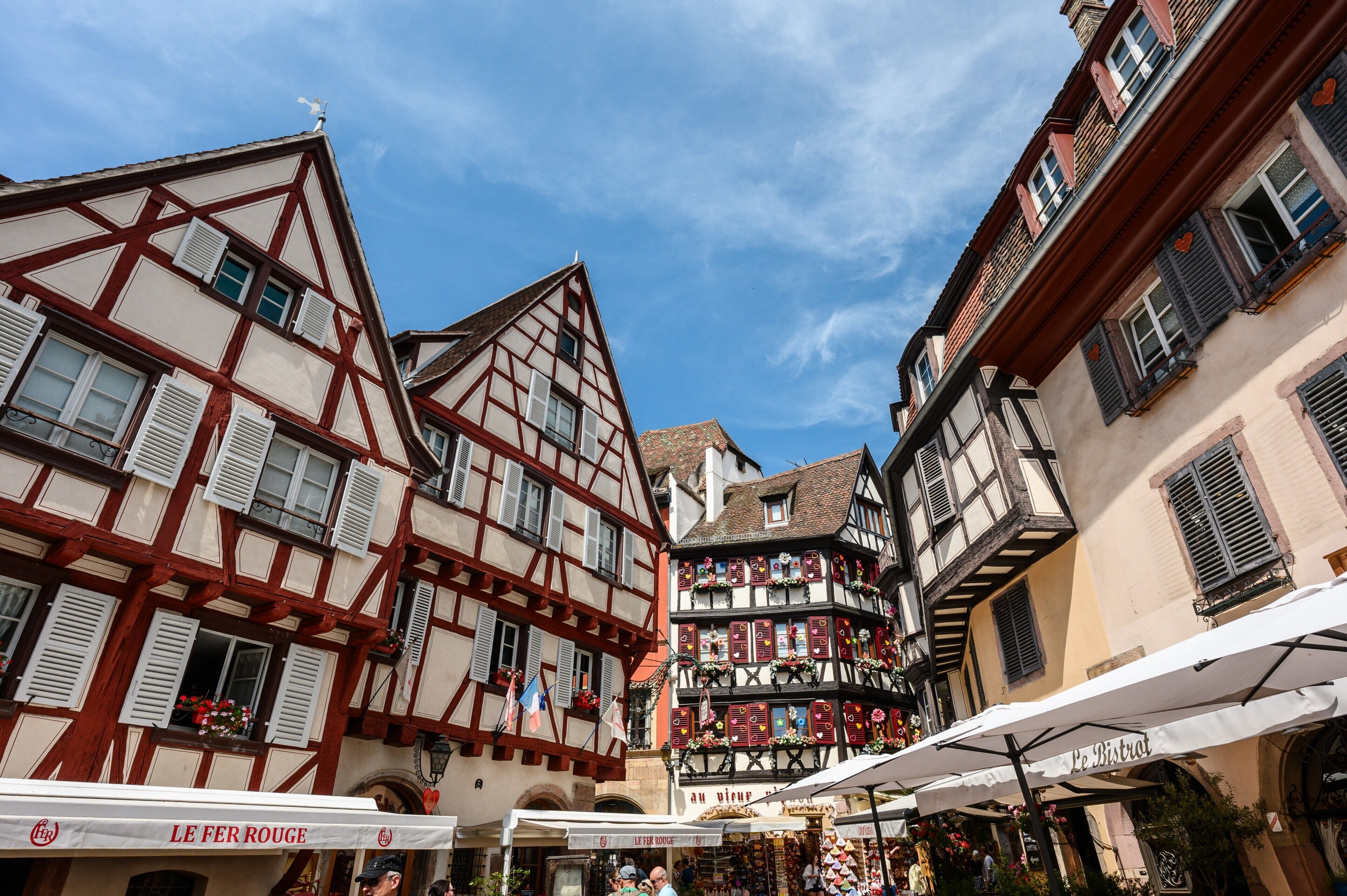 A traditional European street with half-timbered buildings, outdoor cafes, and a clear blue sky.