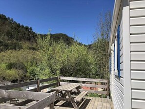 Eine Holzterrasse mit Tisch und Bänken, die auf einen bewaldeten Hang blickt.