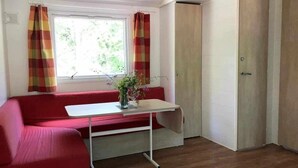 Una habitación con un sofá rojo, una mesita con un florero, una ventana con cortinas y una puerta.