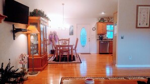 Un salon spacieux avec une table à manger en bois, des chaises et un téléviseur fixé au mur.