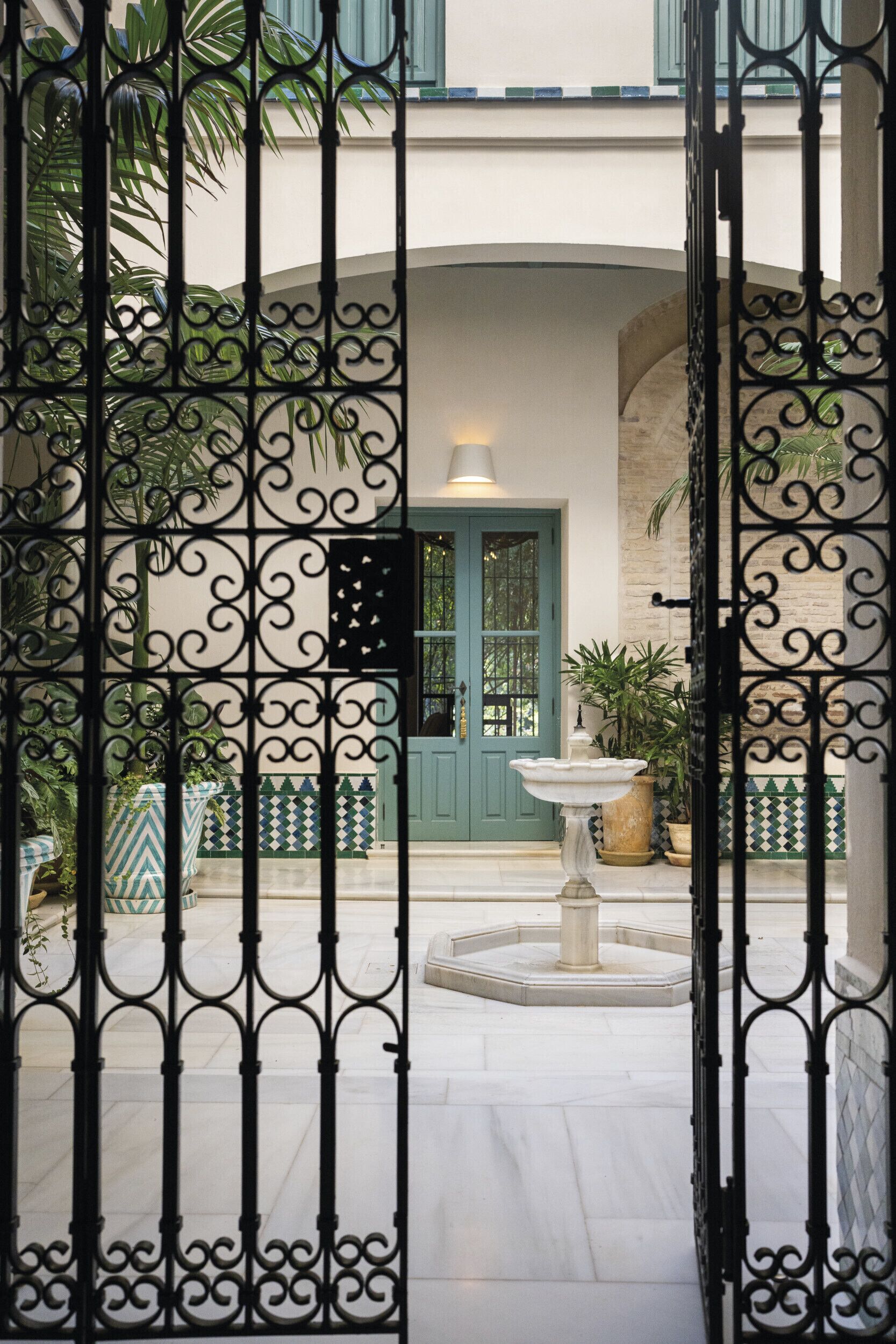 Un cortile con una porta verde, una fontana e piante in vaso.