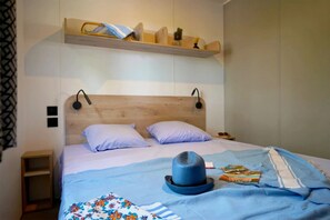 Ein Bett mit Holz-Kopfbrett, zwei Kissen, einer blauen Decke, einem Hut und einem Buch.