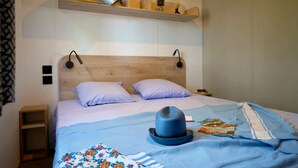 Ein Bett mit Holz-Kopfbrett, zwei Kissen, einer blauen Decke, einem Hut und einem Buch.