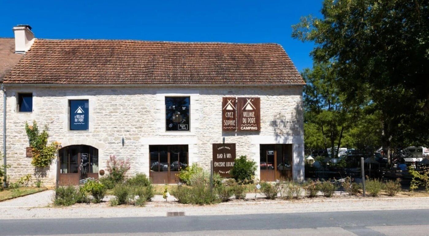 Un bâtiment en pierre avec des enseignes indiquant « Chez Village », « Sophie du Port » et « Camping ».