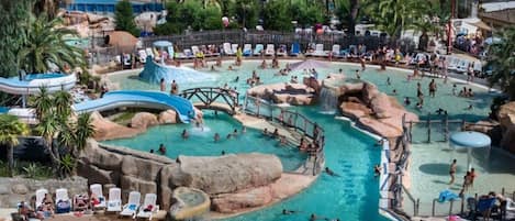 Uma grande piscina ao ar livre com vários elementos aquáticos, incluindo toboáguas e formações rochosas.