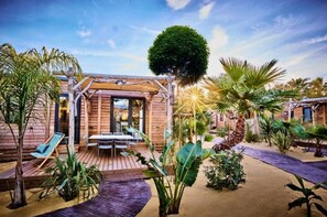 Eine Holzhütte mit einer Terrasse, einer überdachten Sitzgelegenheit und einem großen Baum.
