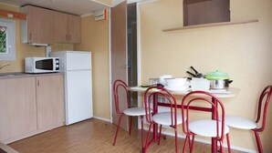 A compact kitchen with a microwave, refrigerator, and a dining area with four red chairs. - Camping 3 étoiles - Piscine  - ccbgcii (Lavelanet)