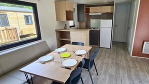 A compact kitchen with a dining area, a window with a view, and a door leading to another room. - Camping 3 étoiles - Piscine  - ccbgcii (Lavelanet)