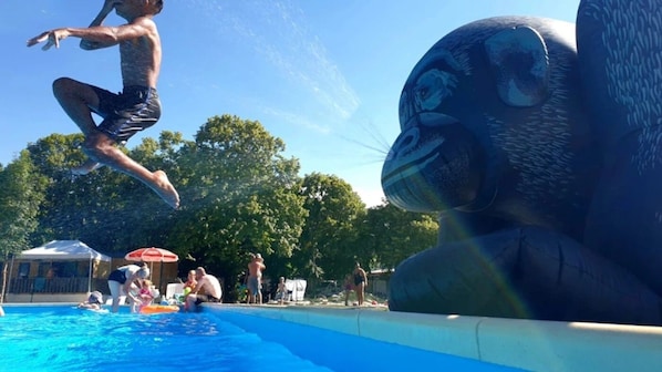 Eine Person springt in einen Pool, im Hintergrund ist eine große Skulptur eines Tieres zu sehen.