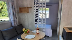 A compact room with a dining table set for two, a sofa, a bed, and a small kitchen area. - Camping 4 étoiles - Parc aquatique - ccbgde0 (La Baule)