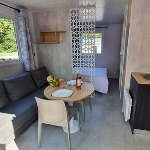 A compact room with a dining table set for two, a sofa, a bed, and a small kitchen area. - Camping 4 étoiles - Parc aquatique - ccbgde0 (La Baule)