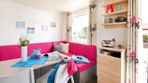 A cozy room with a pink sofa, a table with a vase of flowers, and a radio on a shelf. - Camping 4 étoiles - Parc aquatique - ccbgde0 (La Baule)