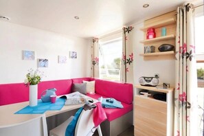 A cozy room with a pink sofa, a table with a vase of flowers, and a radio on a shelf. - Camping 4 étoiles - Parc aquatique - ccbgde0 (La Baule)