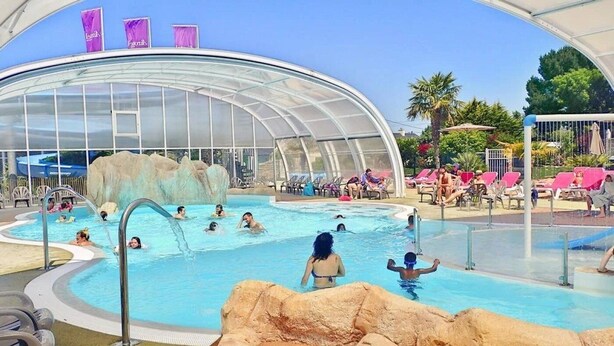 A pool area with a glass-enclosed structure, lounge chairs, and a water slide. - Camping 4 étoiles - Parc aquatique - ccbgdea (La Baule)
