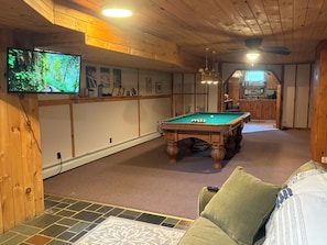 A pool table in a room with wooden walls, a television mounted on the wall, and a ceiling fan.