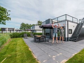 Ein moderner Außenbereich mit Terrassengestaltung, Glasveranda, Gartenmöbeln und einer Treppe zu einer erhöhten Ebene.