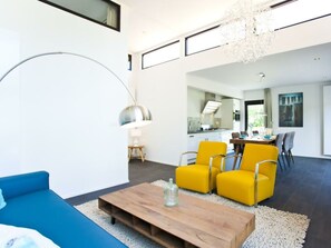 A modern living room with a blue sofa, yellow chairs, a wooden coffee table, and a dining area in the background. - Holiday Home in Breskens With Terrace (Breskens)