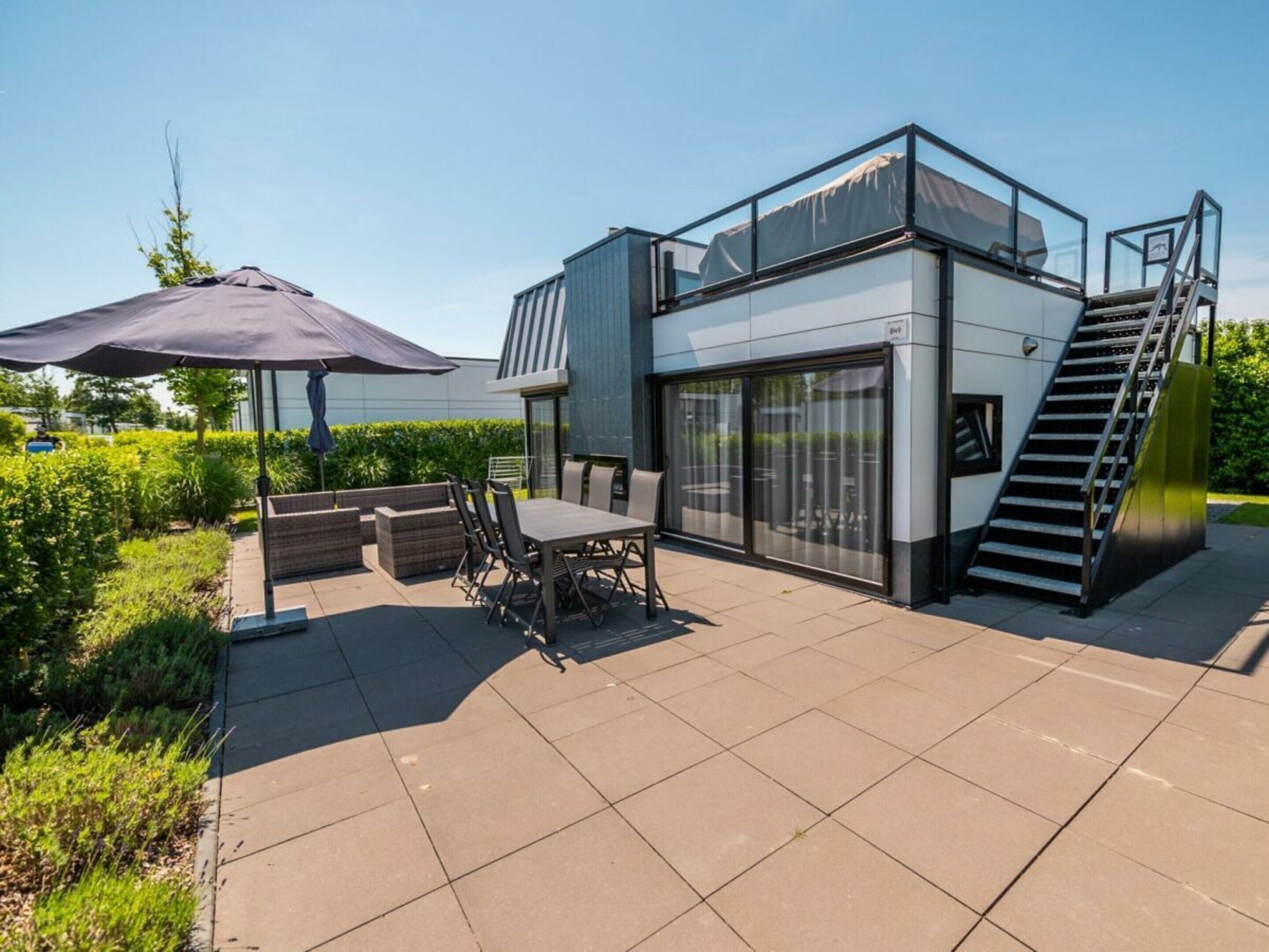 En moderne udendørs terrasse med spiseplads, et overdækket siddeområde og en trappe op til en etage.