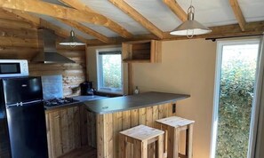 Une cuisine avec des meubles de rangement en bois, un rĂ©frigĂ©rateur noir, une cuisiniĂšre et une fenĂȘtre.
