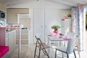 Eine moderne Küche mit weißen Schränken, einer Mikrowelle und einem Gasherd. Es gibt einen Essbereich mit Tisch und Stühlen, eine rosa Vase mit Blumen und ein Fenster mit gemusterten Vorhängen.