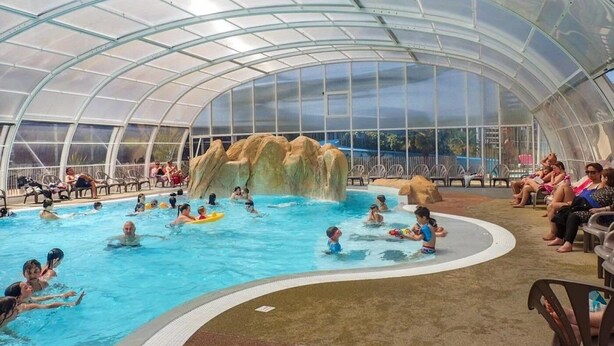 Una piscina coperta con cascata, circondata da poltrona relax e un tetto in vetro.