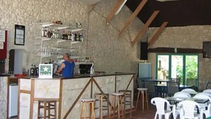 A bar area with stools, a counter, and shelves with bottles. - Camping 3 étoiles - Piscine  - ccbfi0d (Mauroux)
