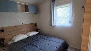 Una camera da letto con un letto, una finestra con tende, una testiera in legno e un piccolo ripiano.
