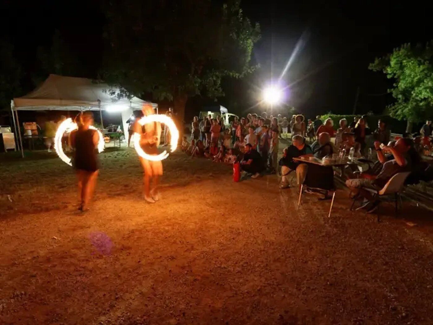 Evento al aire libre con gente reunida, algunos sentados y otros de pie, bajo una carpa.
