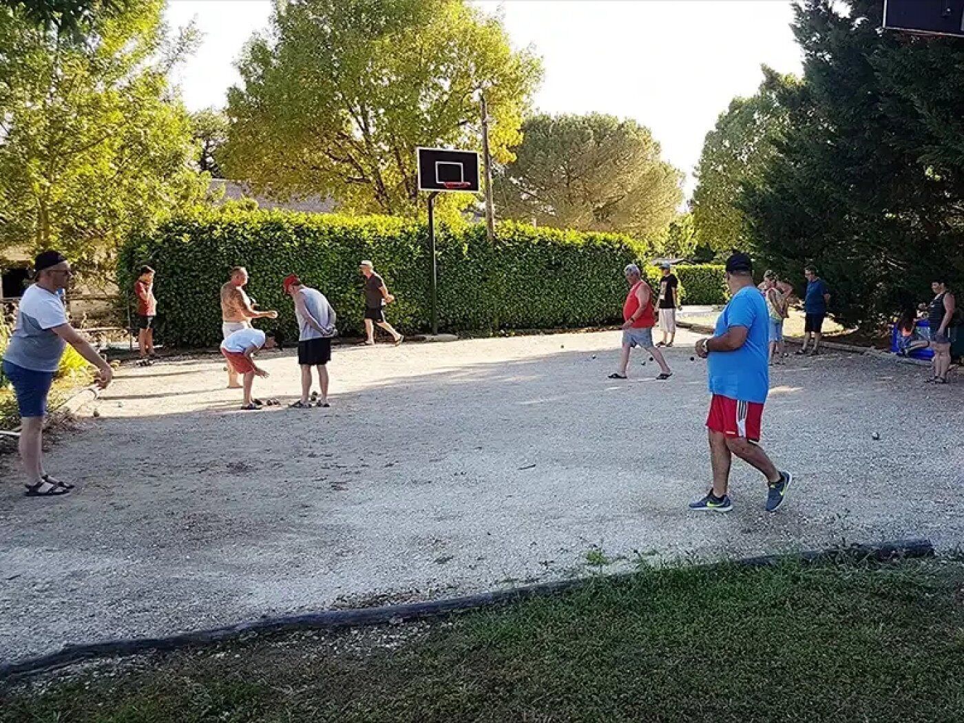 An outdoor area with a basketball hoop, gravel ground, and people engaged in activities.