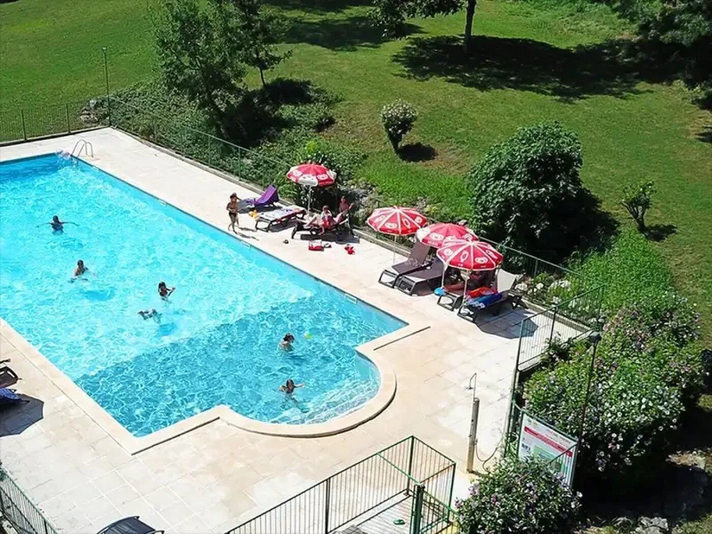 An aerial view of a swimming pool with a few people in the water, surrounded by lounge chairs and umbrellas.