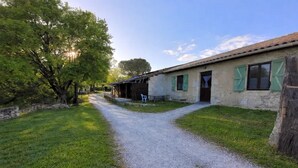 Un edificio in pietra rustica con un vialetto ghiaioso che vi conduce, immerso nel verde.