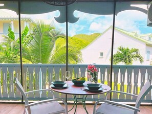 A balcony with a table set for two, a bowl of fruit, and a vase of flowers. - Palmaya · Cozy tropical retreat, beach & pool (Anse Marcel)