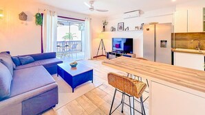 Un salon moderne comprenant un canapé, une table basse, un téléviseur et un balcon aménagé avec du mobilier d’extérieur.
