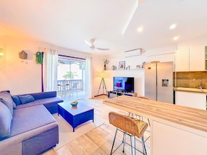 A modern living room with a sofa, coffee table, TV, and a balcony with outdoor furniture. - Palmaya · Cozy tropical retreat, beach & pool (Anse Marcel)
