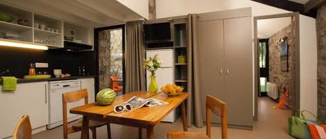 Una cocina moderna con comedor, sillas de madera, una mesa con sandía y flores, y una pared de piedra.