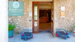 A stone building entrance with a sign for 'Terres de France Domaine des Vans' and two small blue carts. - Camping 3 étoiles - Piscine  - ccbc0gc (Chambonas)