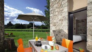 An outdoor dining area with a table set for two, a large umbrella, and a stone wall. - Camping 3 étoiles - Piscine  - ccbc0gc (Chambonas)