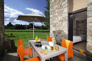 An outdoor dining area with a table set for two, a large umbrella, and a stone wall. - Camping 3 étoiles - Piscine  - ccbc0gc (Chambonas)
