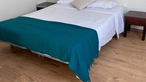 Una cama individual con un edredón color turquesa, ropa de cama blanca y una almohada estampada. Hay dos mesitas de noche con lámparas.