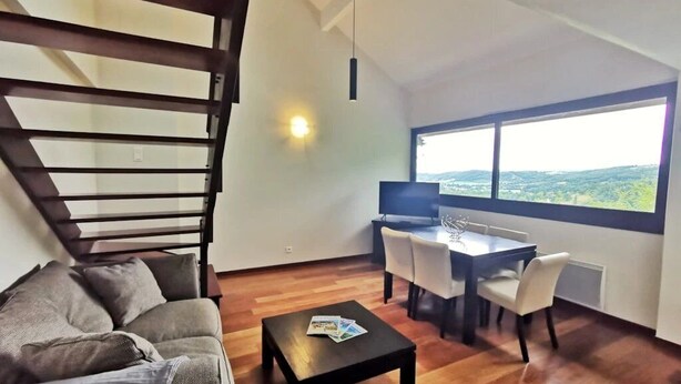 Una sala de estar moderna con sofá, mesa de centro, mesa de comedor, sillas, una escalera y un ventanal con vistas.