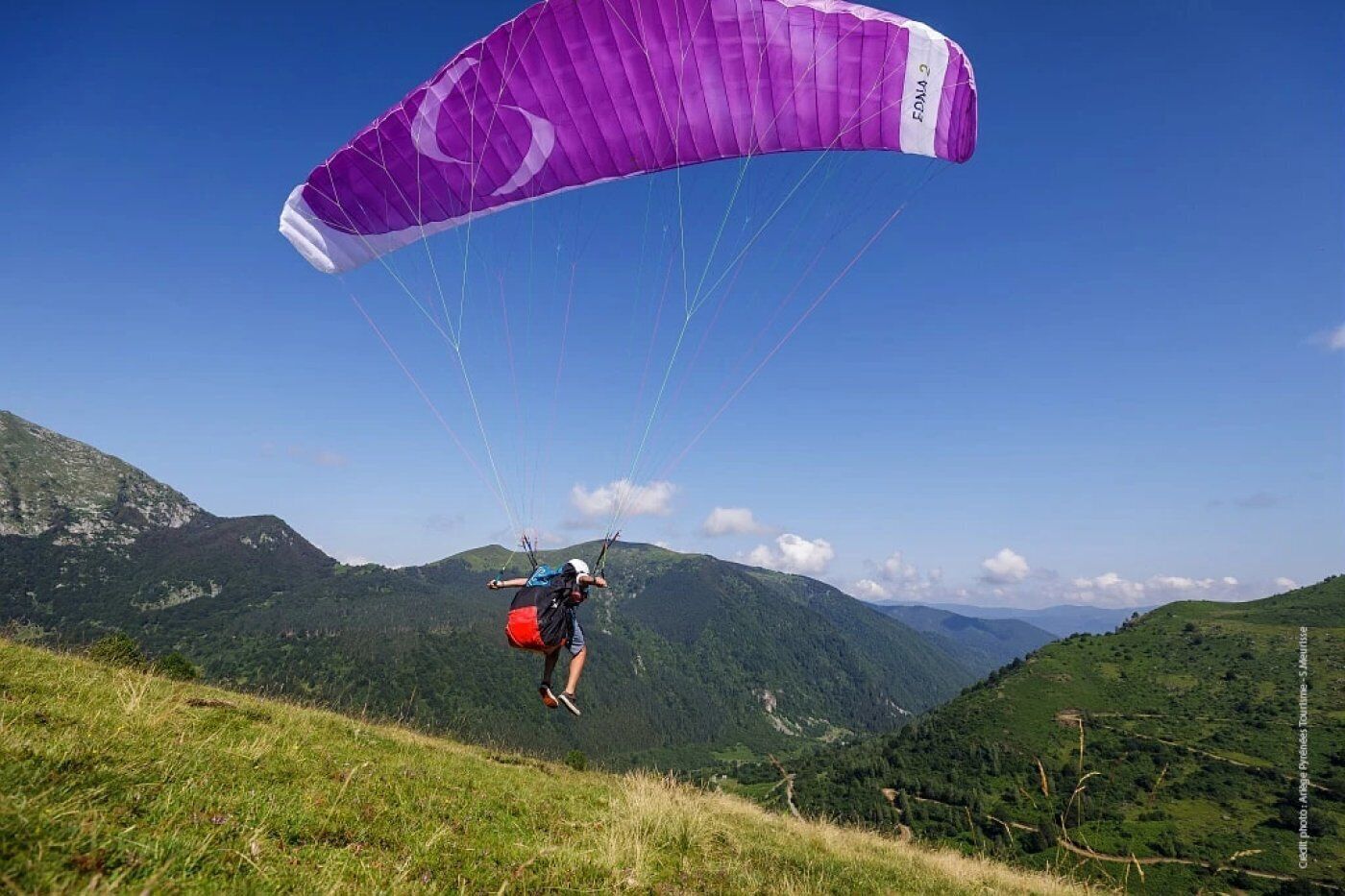 A person paragliding over a mountainous landscape with a purple canopy.