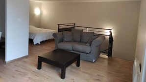 Una habitación pequeña y poco amueblada, con un sofá, una cama y una mesita de centro.