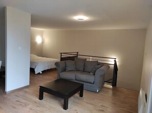 Ein schlichter Raum mit einer Schlafcouch, einem Bett und einem Couchtisch.