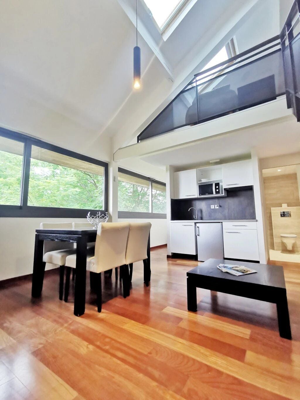 Ein modernes Interieur mit Essbereich, Küche und einem großen Fenster mit Blick auf Grünflächen.