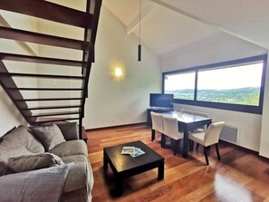 Ein modernes Wohnzimmer mit Sofa, Couchtisch, Esstisch, Stühlen, einer Treppe und einem großen Fenster mit Blick.