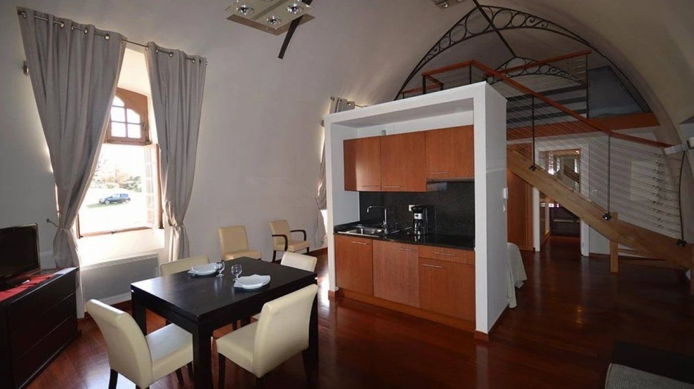 Un comedor con una mesa y sillas, una cocina con armarios de madera y una escalera que lleva a un nivel superior.